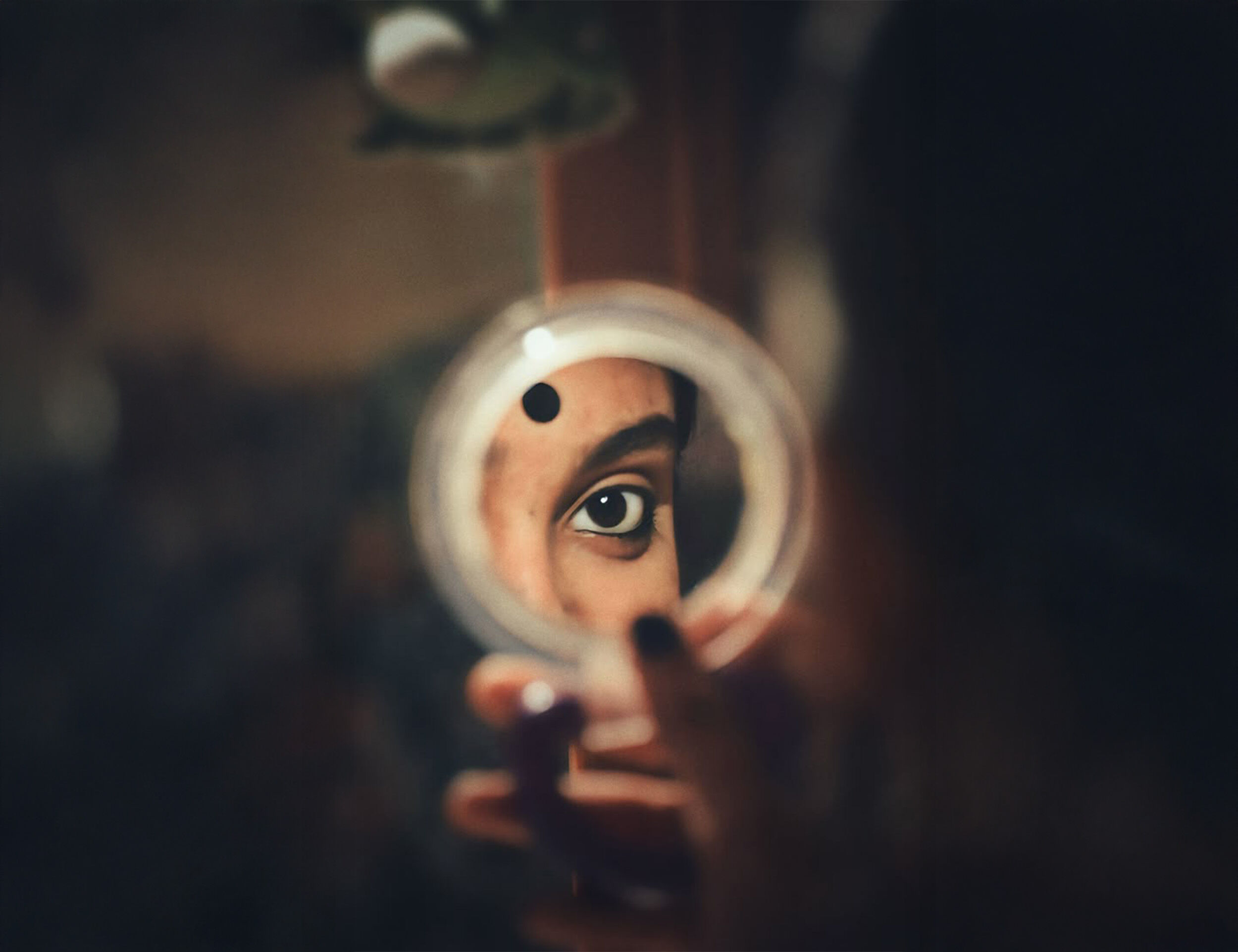 A woman applying a bindi while looking into a small mirror, highlighting the elegance of bindi styles and designs for different face shapes.